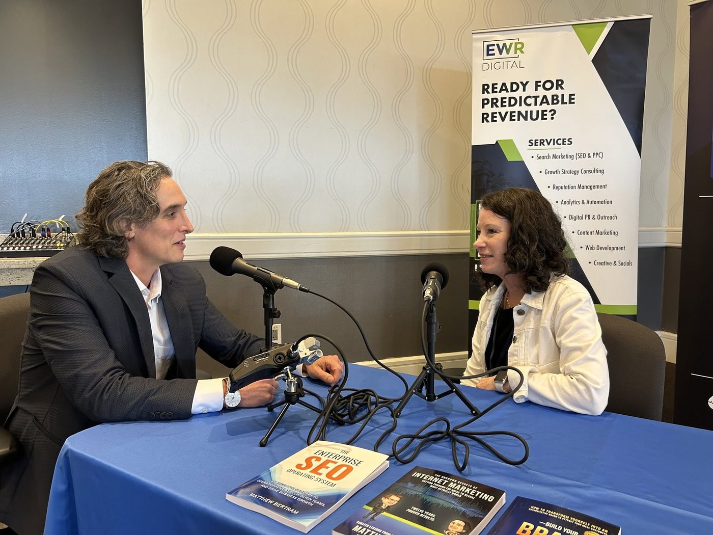 Matthew Bertram interviewing a guest, with his books on the table